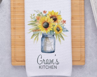 May include: White kitchen towel with a watercolor design of sunflowers in a mason jar. The text "Gram's Kitchen" is printed below the design.