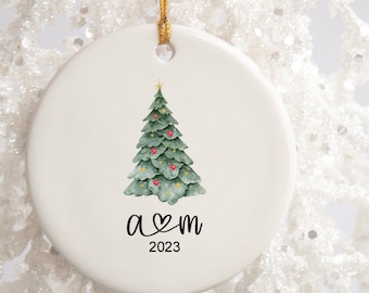 May include: White ceramic Christmas ornament with a green watercolor Christmas tree and red ornaments. The ornament has the text "a ♥ m 2023" printed on it.