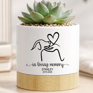 May include: A white ceramic planter with a bamboo base, featuring a succulent plant. The planter has a black line drawing of a dog and heart, with the text "in loving memory" and the name "STANLEY 2015-2026".