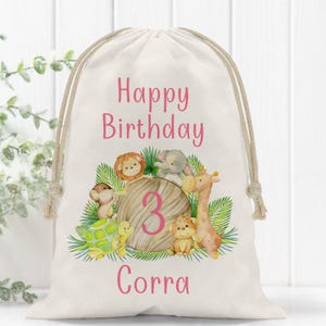 May include: A white canvas gift bag with a pink "Happy Birthday" message, a number "3" surrounded by jungle animals, and the name "Corra" printed on the front.