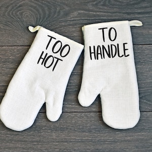May include: A pair of white oven mitts with black text. One mitt says "Too Hot" and the other says "To Handle".