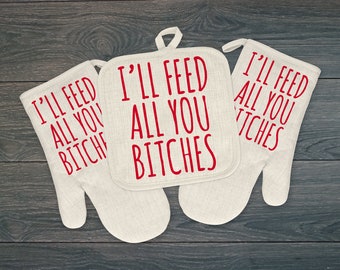 May include: A set of three kitchen textiles: two oven mitts and a square pot holder. All are off-white with the red text "I'LL FEED ALL YOU BITCHES". The mitts have a curved shape, and the pot holder has a loop for hanging.