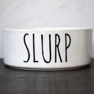 May include: White ceramic pet bowl with the word "SLURP" printed in black.