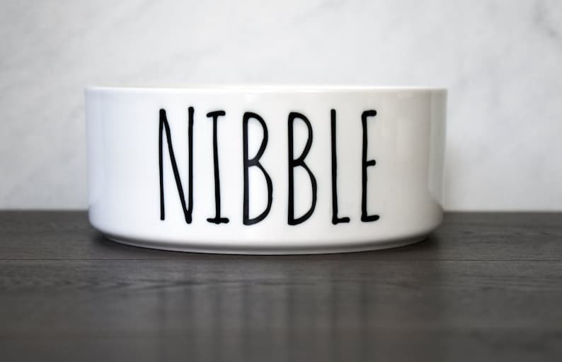 May include: White ceramic pet bowl with the word "NIBBLE" printed in black.