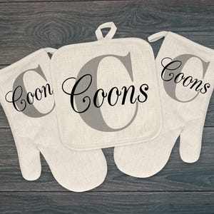 May include: Set of three beige linen pot holders with the word "Coons" printed in black on each. The pot holders are in the shape of a mitten and a square.
