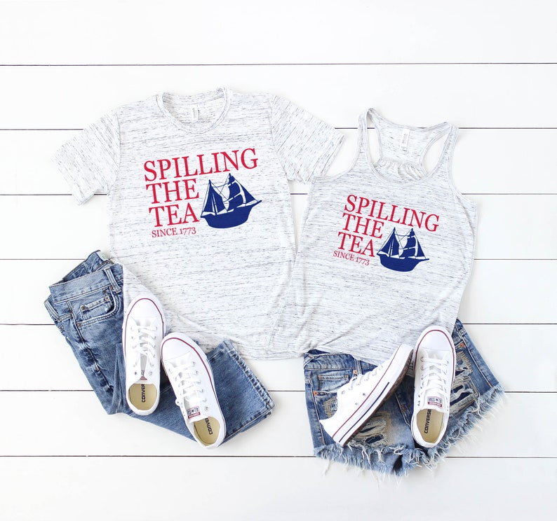 K&ouml;nnte beinhalten: Ein meliertes graues T-Shirt und Tanktop mit dem Text "Spilling the Tea Since 1773" in Rot und Blau, mit einer Segelboot-Grafik. Dazu blaue Jeans, Jeansshorts und wei&szlig;e Turnschuhe.
