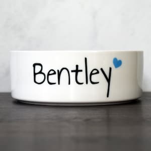 以下が含まれることがあります： 白いセラミック製のペットボウルに、黒い文字で「Bentley」と書いてあり、小さな青いハートが付いています。