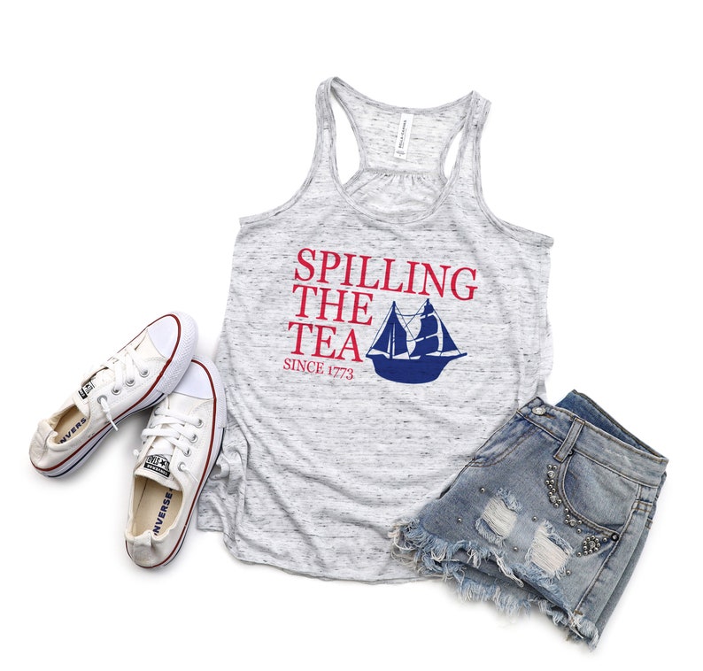 K&ouml;nnte beinhalten: Ein meliertes graues Tanktop mit dem Text "Spilling the Tea Since 1773" und einer blauen Segelboot-Grafik. Das Tanktop wird mit Jeansshorts und wei&szlig;en Converse-Sneakern kombiniert, was ein l&auml;ssiges Outfit ergibt.