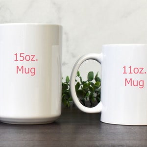 May include: Two white ceramic mugs, one 15oz and one 11oz, with the size printed in pink on the front.