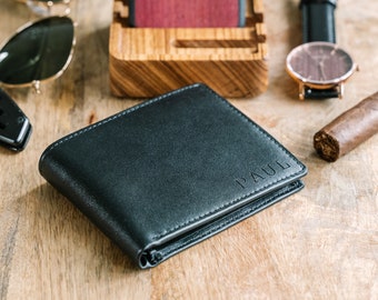 May include: A black leather wallet with the name "PAUL" embossed on the front. The wallet is lying on a wooden surface.