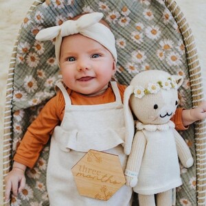 sweet baby girl lying on her baby bassinet together with her adorable bunny stuffed toy covered with the beautiful fall muslin swaddle blanket in the daisy sage green color