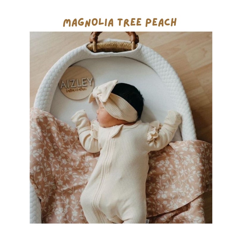 sweet little baby girl lying in her baby basket lined and covered with the magnolia tree peach swaddle blanket perfect for fall babies this fall season and a great gift for babies