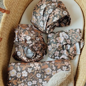 Nursery baby items in a dark floral thicket pattern. A crib sheet, changing pad cover, swaddle and a sherpa faux fur baby blanket. Perfect for fall.