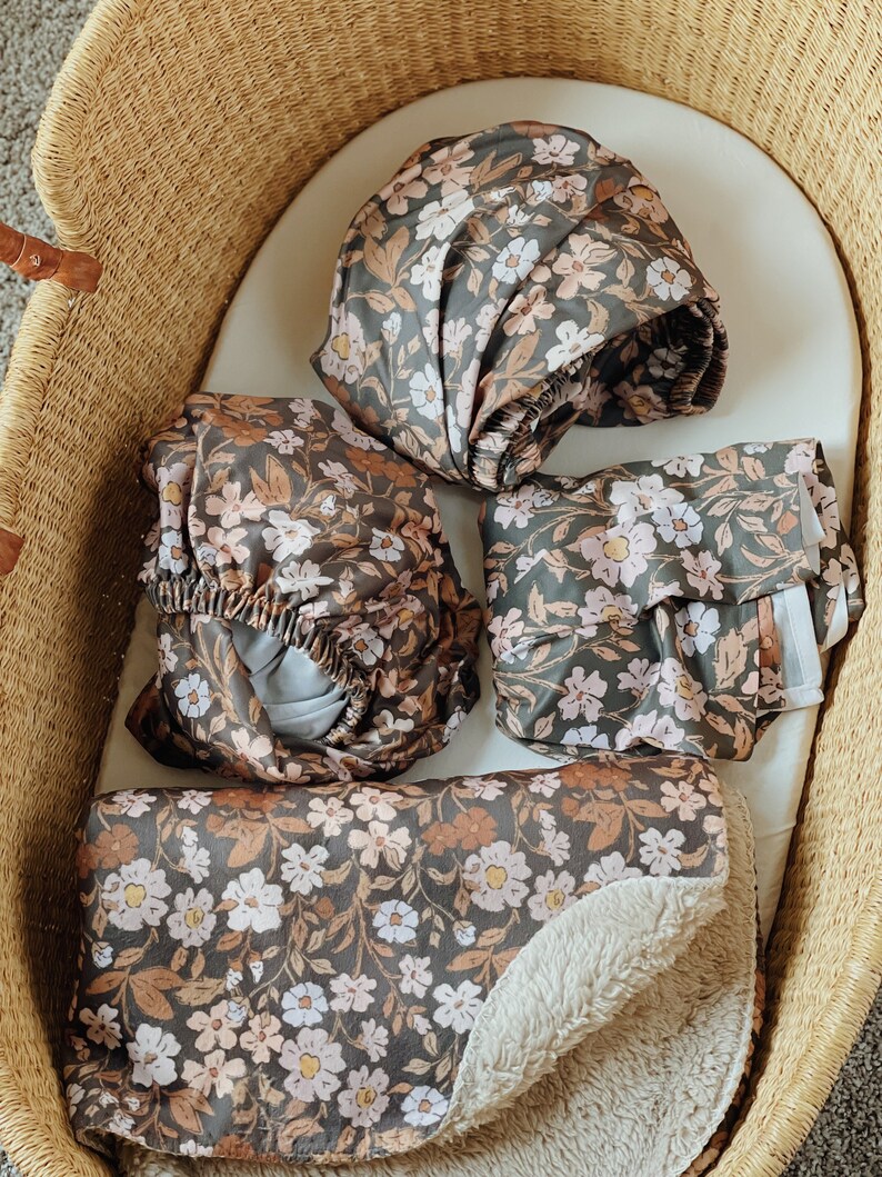 Nursery baby items in a dark floral thicket pattern. A crib sheet, changing pad cover, swaddle and a sherpa faux fur baby blanket. Perfect for fall.