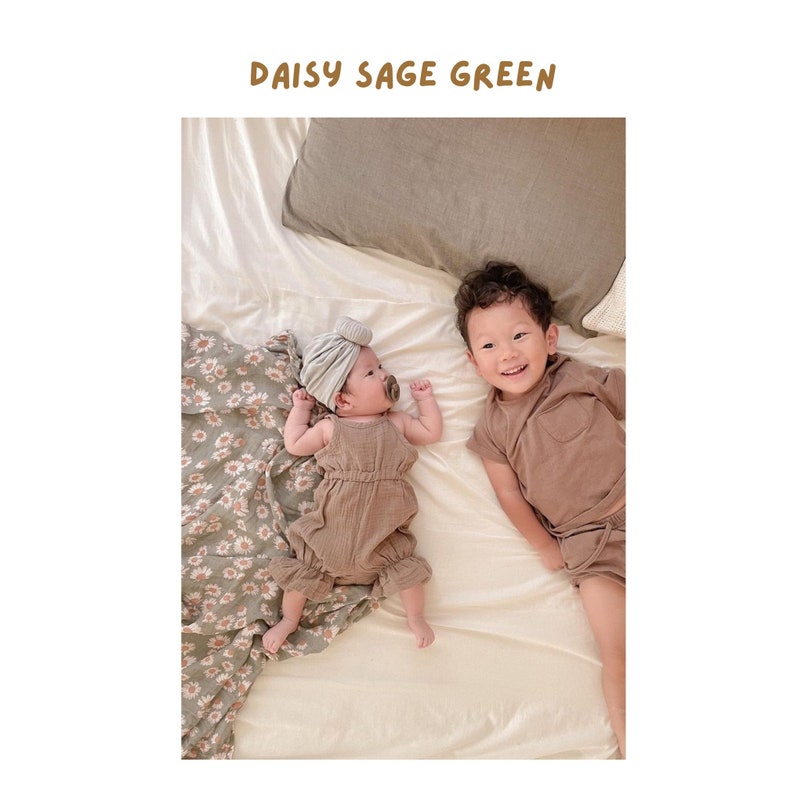 baby girl and baby boy siblings lying in their ultra comfy bed with the daisy sage green muslin swaddle blanket for fall used as a photo backdrop for the baby girl