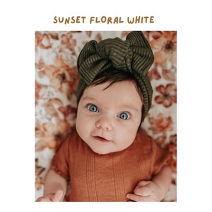 adorable little girl wearing a dark moss green headband smirking and looking into the camera with the fall swaddle blanket sunset floral white used as her background cover or backdrop
