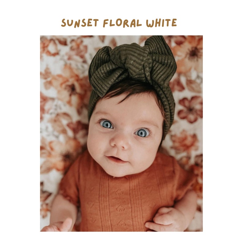 adorable little girl wearing a dark moss green headband smirking and looking into the camera with the fall swaddle blanket sunset floral white used as her background cover or backdrop