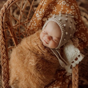 sweet little girl smiling while sleeping doing her photoshoot wearing a brownish yellow wrap using the whimsy floral mustard muslin baby swaddle wrap as her photoshoot backdrop