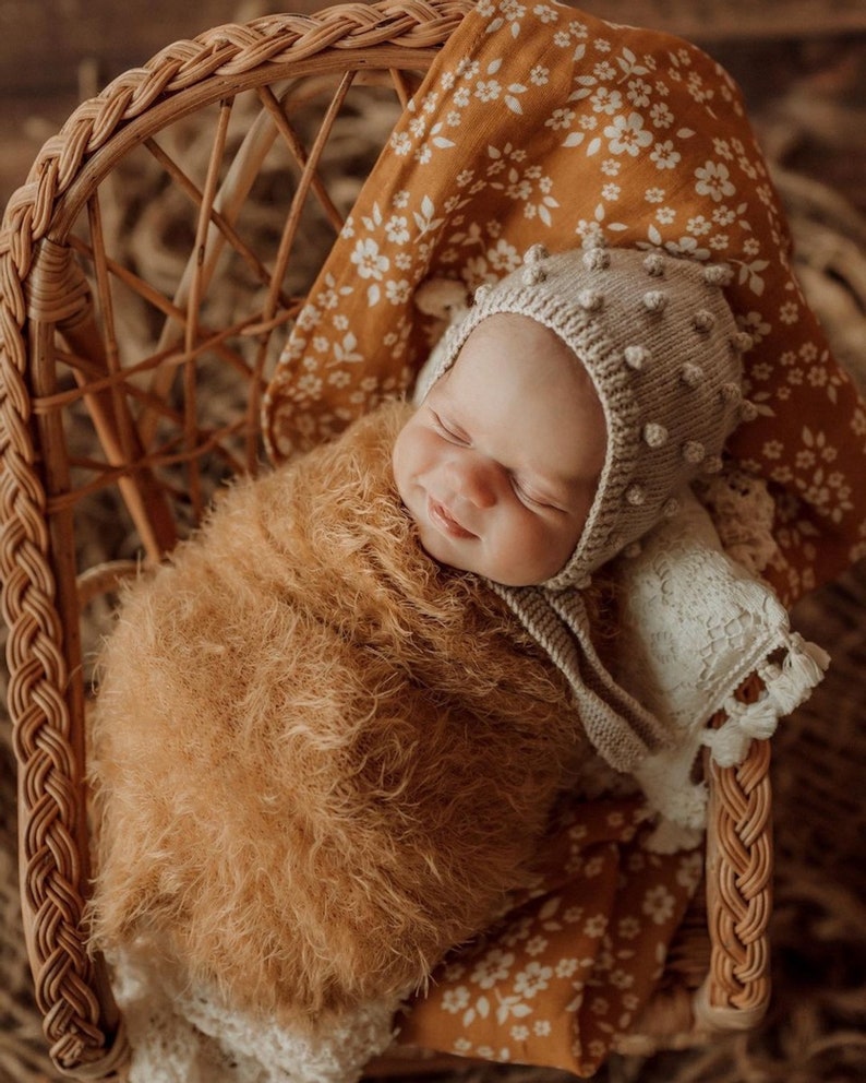 sweet little girl smiling while sleeping doing her photoshoot wearing a brownish yellow wrap using the whimsy floral mustard muslin baby swaddle wrap as her photoshoot backdrop