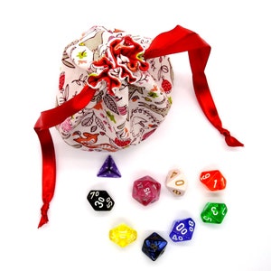 May include: A fabric dice bag with a woodland pattern, tied with a red ribbon, and a collection of colorful polyhedral dice. The bag is cream-colored with a floral and animal print.