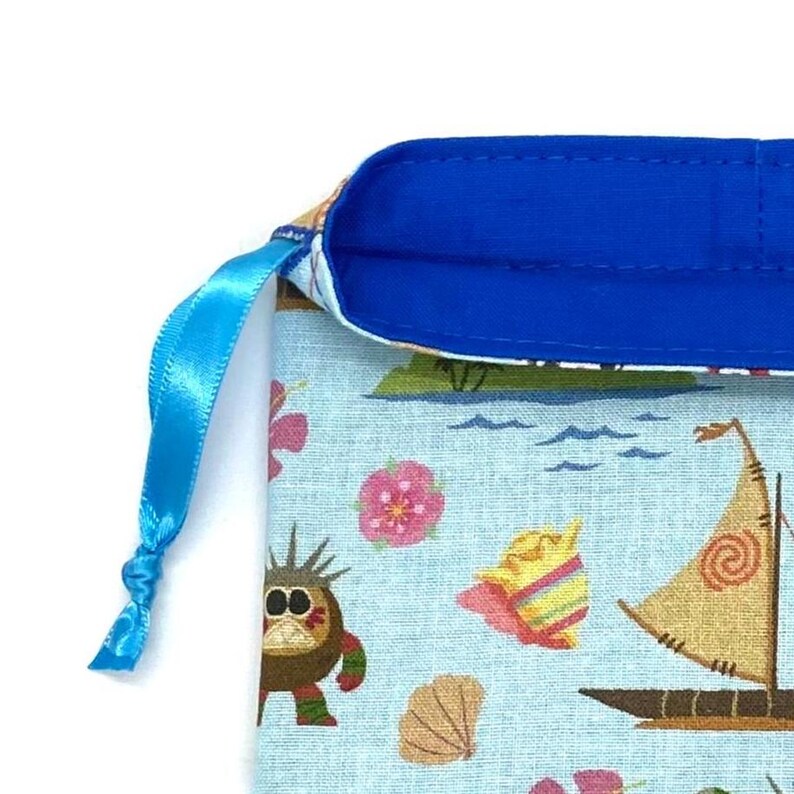 May include: A light blue drawstring bag with a tropical print featuring sailboats, flowers, and cartoon characters. The bag has a bright blue satin ribbon drawstring and a blue interior lining.
