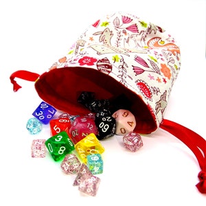 May include: A fabric dice bag with a red interior and a white exterior patterned with pink flowers, rabbits, and other floral elements. A variety of colorful dice are spilling out of the bag, including blue, red, green, and clear dice.