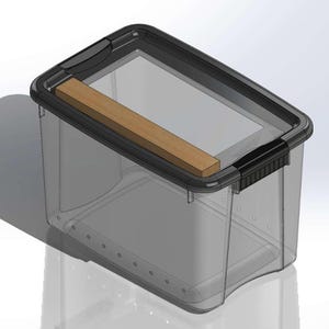 May include: A clear plastic storage bin with a black lid and a wooden plank. The bin has a rectangular shape with rounded corners and small holes along the bottom edge. The lid has a handle on one side.