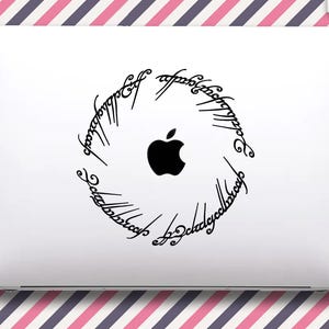 Op de afbeelding: Witte laptop met een zwart Apple-logo in het midden, omcirkeld door een zwart script. De laptop staat op een achtergrond met roze en paarse diagonale strepen.