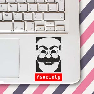 May include: A black and white sticker featuring a stylized face with a large mustache and the word "fsociety" in red text. The sticker is placed on a white laptop, with a keyboard visible. The background has pink and purple diagonal stripes.