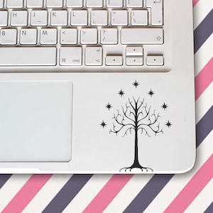 Op de afbeelding: Een zwarte sticker van een boom met sterren op een witte laptop. De boom heeft een lange stam, takken en wortels. De laptop staat op een oppervlak met roze, witte en paarse diagonale strepen.