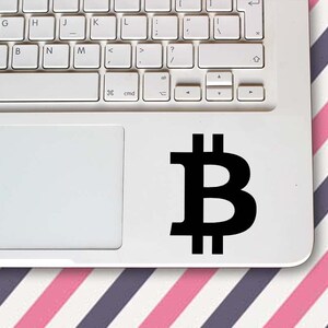 May include: A white laptop computer with a black Bitcoin symbol sticker on the trackpad.