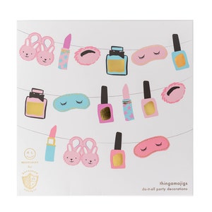 May include: A white card featuring a string of illustrated party decorations. The decorations include pink bunny slippers, lipsticks with star patterns, nail polish, eye masks, and powder puffs. The card also includes the text "HELLO!LUCKY for DAYDREAM SOCIETY" and "thingamajigs do-it-all party decorations."