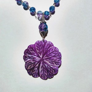 Pu&ograve; includere: Una collana con un ciondolo a forma di fiore viola, una catena d'argento e perline di vetro blu e viola.
