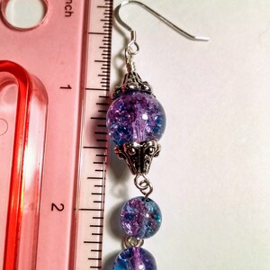 Pu&ograve; includere: Orecchini pendenti in argento con tre perline di vetro blu e viola. La perlina superiore presenta un design in filigrana d'argento. Gli orecchini sono lunghi circa 5 cm.