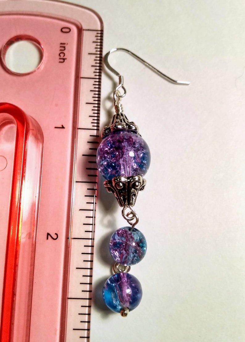 Pu&ograve; includere: Orecchini pendenti in argento con tre perline di vetro blu e viola. La perlina superiore presenta un design in filigrana d'argento. Gli orecchini sono lunghi circa 5 cm.