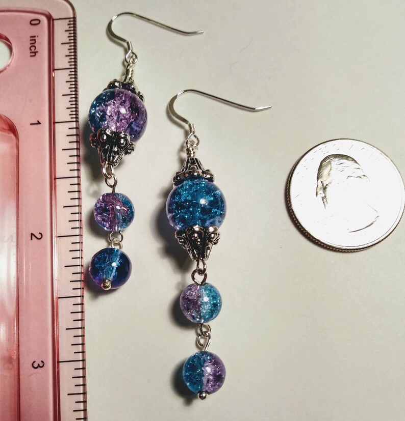 Pu&ograve; includere: Un paio di orecchini pendenti con perline d'argento e perline di vetro blu e viola. Gli orecchini sono lunghi circa 5 cm.
