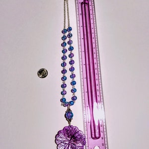Pu&ograve; includere: Una collana di perline di vetro blu e viola con un grande ciondolo a forma di fiore viola. La collana &egrave; lunga 71 cm e ha una chiusura argentata.