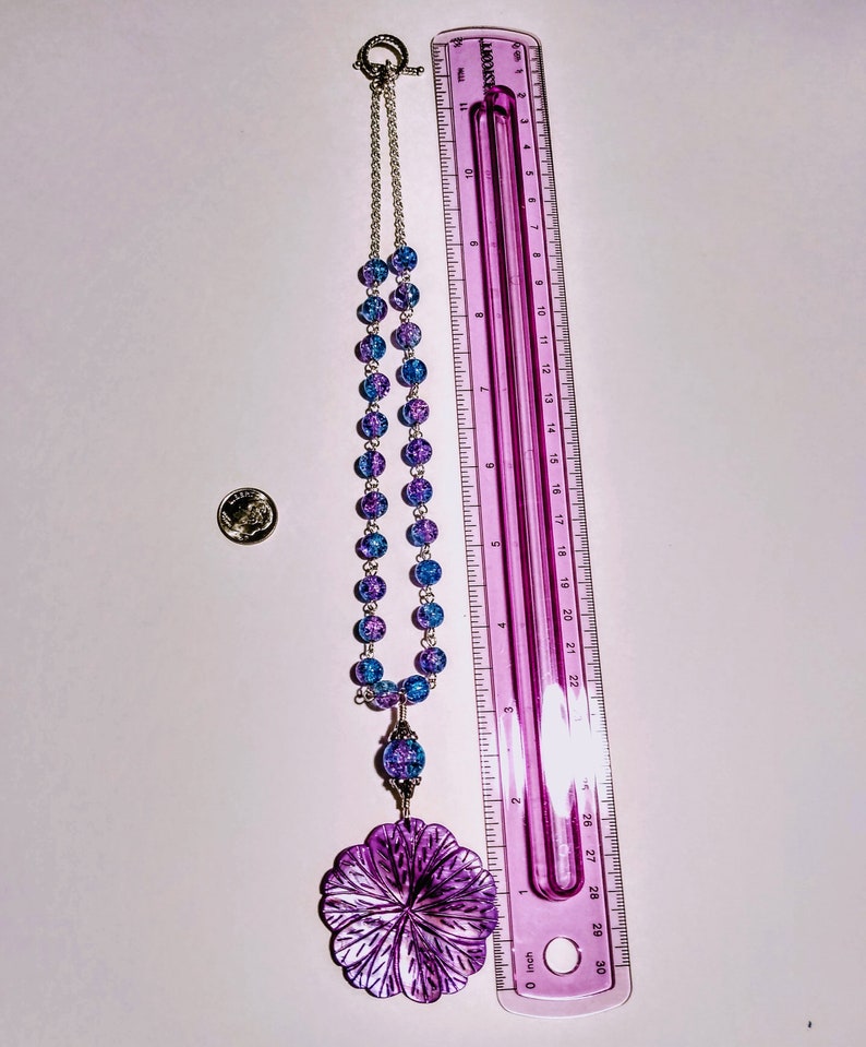 Pu&ograve; includere: Una collana di perline di vetro blu e viola con un grande ciondolo a forma di fiore viola. La collana &egrave; lunga 71 cm e ha una chiusura argentata.