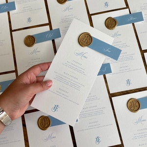 Menú de boda y tarjetas de presentación en azul polvoriento con sello de lacre dorado. Impreso en cartulina martillada