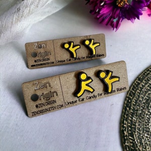 Puede incluir: Dos pares de pendientes de madera con contorno negro y diseño de figura amarilla. Los pendientes están sobre una tarjeta marrón con el texto "Zen Origin" y "Unique Ear Candy for Badass Babes".