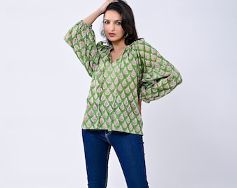 May include: A green and pink floral print blouse with a V-neck and long sleeves. The blouse has a gathered detail at the neckline and a tie at the front. The model is wearing blue jeans and clear heeled sandals.
