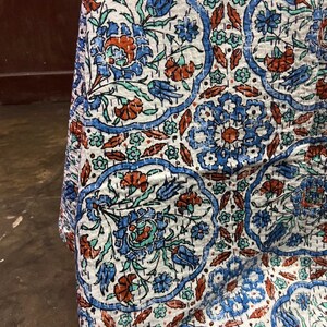 May include: A white cotton quilt with a blue and orange floral pattern. The quilt is quilted in a traditional style with small stitches.
