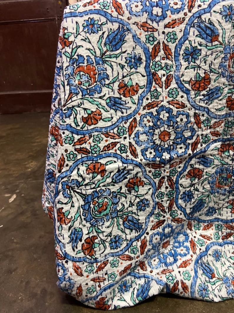 May include: A white cotton quilt with a blue and orange floral pattern. The quilt is quilted in a traditional style with small stitches.