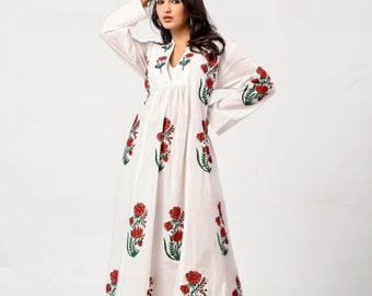 Op de afbeelding: Witte maxi-jurk met een bloemenprint met rode bloemen en groene bladeren. De jurk heeft een V-hals en lange mouwen.