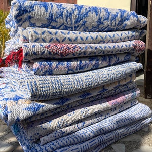 May include: A stack of eight kantha quilts in shades of white and blue with a few red accents. The quilts are made of cotton and have a hand-stitched design.
