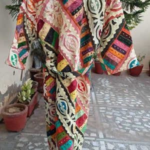 May include: A colorful patchwork robe with a white background and black geometric patterns. The robe has a long, flowing silhouette and a tie belt.