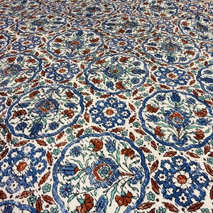 May include: A white fabric with a blue and brown floral pattern. The pattern features intricate designs with repeating motifs of flowers and leaves.