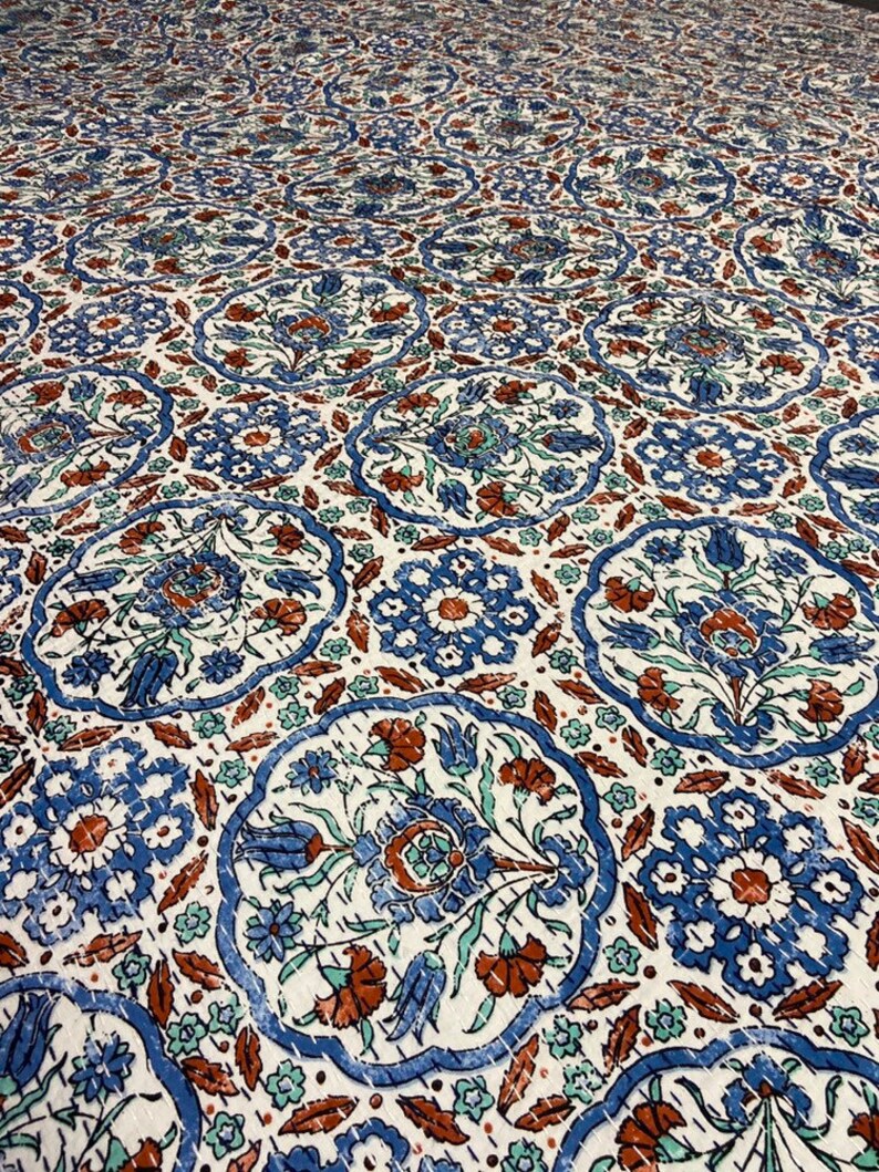 May include: A white fabric with a blue and brown floral pattern. The pattern features intricate designs with repeating motifs of flowers and leaves.