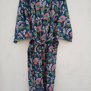 May include: A blue cotton robe with a floral print featuring pink, green, and white flowers. The robe has a tie belt and long sleeves.