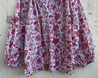 May include: A white blouse with a pink floral print and a tie at the neck. The blouse has long sleeves with a gathered cuff.